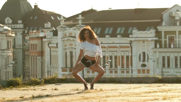 Una mujer joven con piernas largas en pantalones cortos pequeños que realizan un baile atractivo en el techo bajar y extender sus piernas- puesta de sol brillante — Vídeo de stock