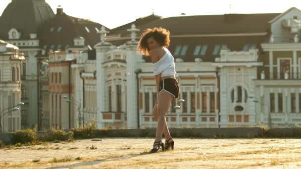 Une jeune femme aux longues jambes en petit short exécutant une danse attrayante sur le toit - descendant montrant ses étirements - coucher de soleil lumineux — Video