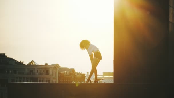 Una joven con el pelo rizado realizando un baile de striptease atractivo sobre un fondo de edificios - puesta de sol — Vídeos de Stock