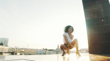 Kıvırcık saçlı genç bir kadın modern binaların arka planda çekici dans yapıyor - gün batımı