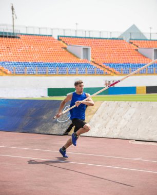 Sırıkla atlama - genç bir adam stadyumda bir kutup tutarak çalışır