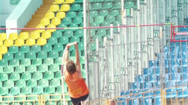 Bóveda de poste: un hombre con camisa naranja salta sobre la barra — Vídeos de Stock