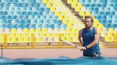Sırıkla atlama - esnek bir kutup kullanarak bar üzerinden atlama mavi gömlek sakallı atletik adam