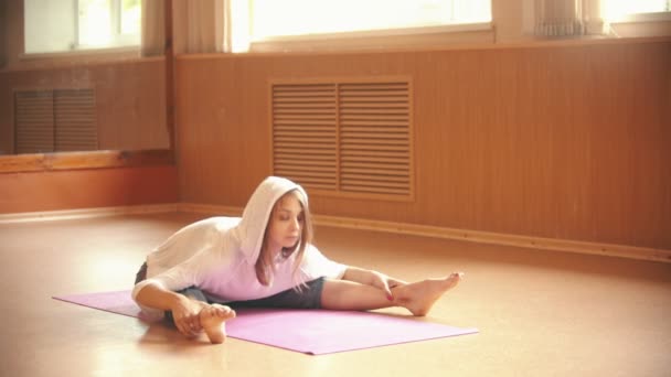 Giovane donna che si riscalda seduta sul pavimento e fa esercizi di stretching - piegandosi al pavimento - studio di danza alla luce del giorno — Video Stock