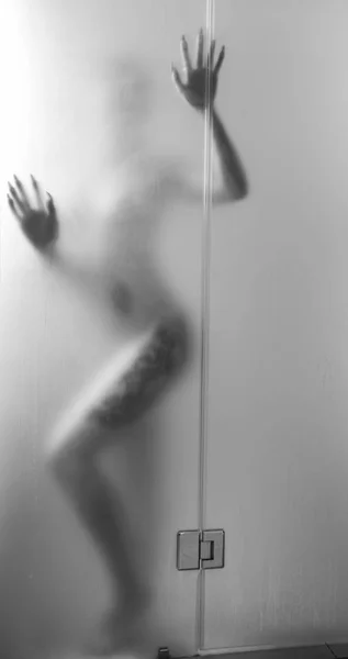 Uma mulher sexy com tatuagens em pé no banheiro atrás da cabine do chuveiro uma silhueta atrás de vidro fosco — Fotografia de Stock