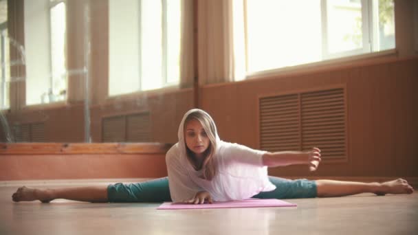 Joven mujer bonita sentada en la esterilla de yoga realizando una división inclinándose hacia el suelo — Vídeos de Stock