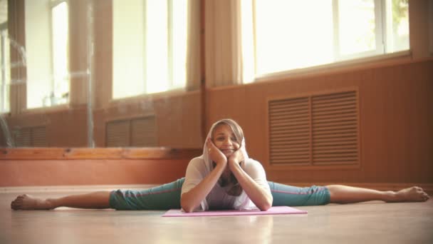 Jonge mooie vrouw zittend op de yoga mat uitvoeren van een split-rekwisieten op het gezicht met haar handen en op zoek-Dance Studio — Stockvideo