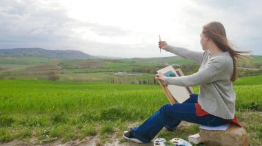 Yetenekli bir kadın sahada oturur ve çizim - bir fırça ile oranlarını ölçer