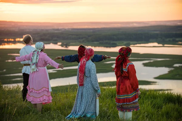 伝統的なロシアの服を着た人々が野原に立ち、夕日を眺めている — ストック写真