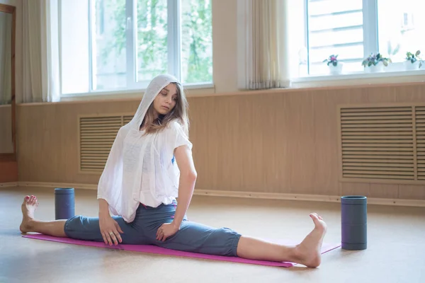 Joven mujer delgada con el pelo rubio sentado en la esterilla de yoga en división horizontal - estudio de baile — Foto de Stock