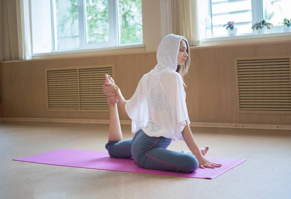 Fiatal karcsú nő ül a jóga mat, és ezzel nyújtó gyakorlatok-húzza a lábát, hogy a test — Stock Fotó