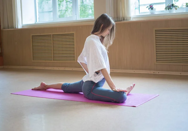 Joven mujer delgada con cabello rubio sentada en la esterilla de yoga y haciendo ejercicios de estiramiento —  Fotos de Stock