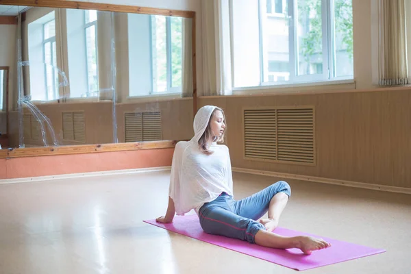 Jonge slanke vrouw met blond haar zittend op de yoga mat in dansstudio en op zoek naar de zijkant — Stockfoto