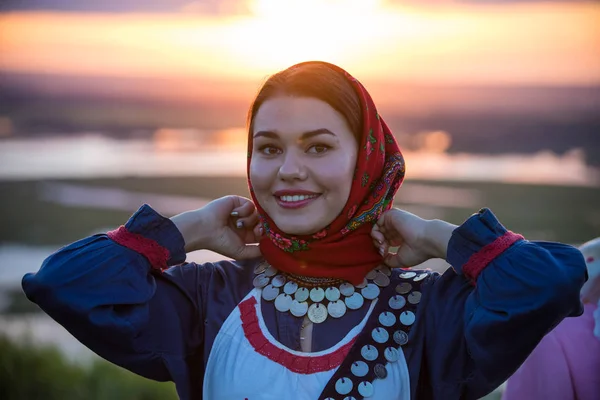 Joven mujer bastante sonriente en ropa tradicional rusa sobre un fondo de la puesta del sol —  Fotos de Stock