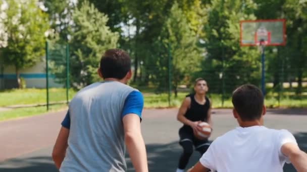 Tre idrottsmän spela basket på domstolen utomhus-en man kastar bollen — Stockvideo