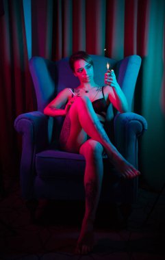 Seksi bir iç çamaşırı genç kadın çapraz bacaklar ile bir sandalyede oturan ve çakmak kadar hafif tutarak