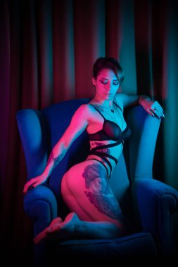 Neon aydınlatma bir sandalyede oturan seksi bir iç çamaşırı birçok dövme ile genç kadın