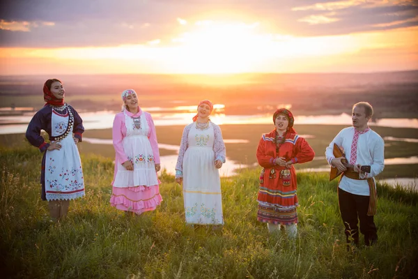 People in traditional russian clothes standing on the field on a background on the bright sunset - sing the song — Stock Photo, Image