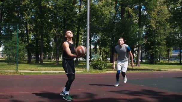 Δύο νέοι άντρες που παίζουν μπάσκετ στην ύπαιθρο-ένας άνθρωπος που πετάει την μπάλα-άλλος άνθρωπος σκοράρει — Αρχείο Βίντεο