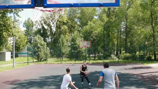 Drei Sportler, die draußen auf dem Platz Basketball spielen - ein Mann in schwarzer Uniform wirft den Ball und trifft — Stockvideo