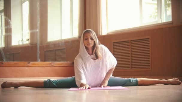 Jonge vrouw in witte losse shirt zittend op de yoga mat het uitvoeren van een split en leunend naar voren-dansstudio — Stockvideo