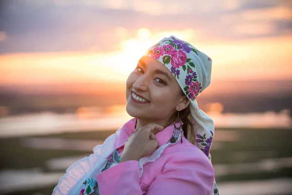 Eine lächelnde Frau in traditioneller Tracht vor dem Hintergrund des hellen Sonnenuntergangs — Stockfoto