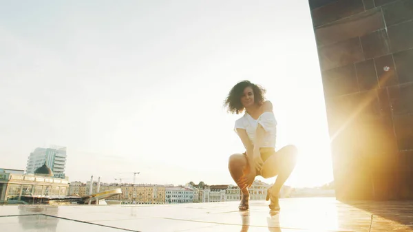 Une jeune danseuse de strip sexy sur des talons hauts montrant des éléments de danse s'assoit sur le squat — Photo