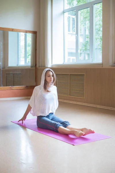 Young slim woman sitting on the yoga mat and pulling her toes forward