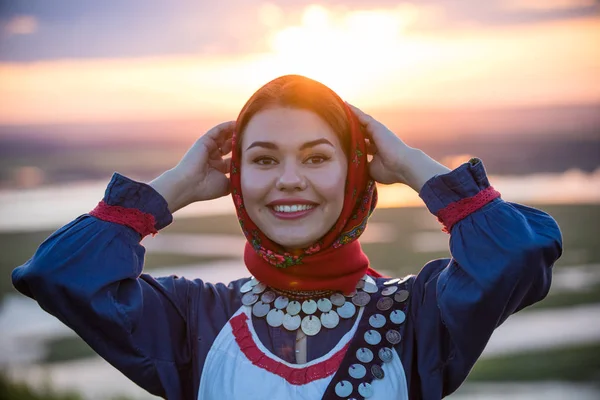 Young smiling woman in traditional russian clothes on a background of the sunset — Stock Photo, Image