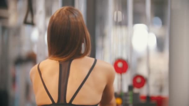 Una atleta entrenando en el gimnasio - tirando de las asas conectadas a piezas de peso - bombeando músculos y manos del pecho — Vídeo de stock