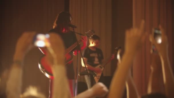 Um jovem com cabelo comprido cantando uma música em sua performance - pessoas acenando com as mãos — Vídeo de Stock