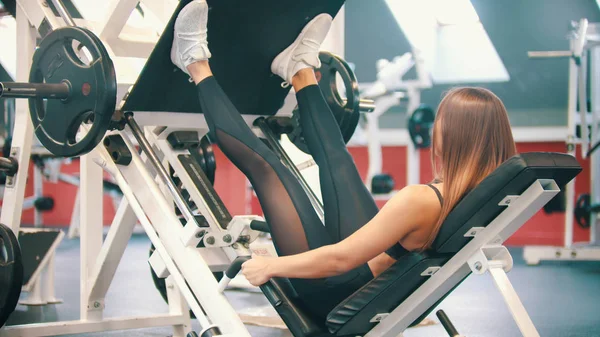 Uma mulher esportiva se exercitando no ginásio - executando uma perna pressionar o aparelho de treinamento — Fotografia de Stock