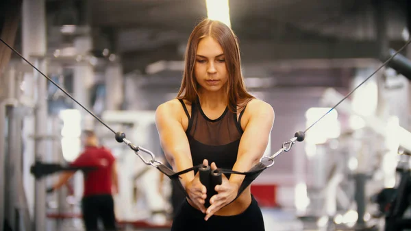 Una mujer deportiva entrenando en el gimnasio - tirando de las asas contra sí misma - entrenando las manos —  Fotos de Stock