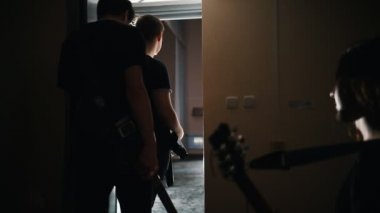 Sahnede yürüyen ve dinleyicilerini selamlayan bir rock grubu elleriyle el sallıyor.