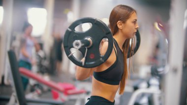 Spor salonunda eğitim bir atlet kadın - dumbbell altında alır ve omuzlarında koymak