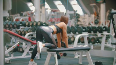 Spor salonunda uzun saç eğitimi ile sportif bir kadın - kollarını eğitim - bir diz ile standında dururken dambıl çekerek