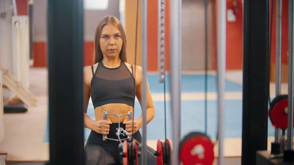 Uma mulher atleta se exercitando no simulador de treinamento no ginásio puxando as alças conectadas a peças de peso — Fotografia de Stock