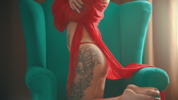 Mladá žena s tetování v sexy červeném prádle, sedící v křesle na kolenou — Stock video