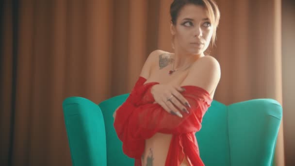 Fiatal nő fényes töltsük fel egy szexi piros fehérnemű ül a széken a térdére — Stock videók