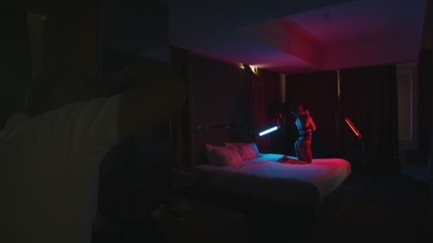 Młoda kobieta w seksownej bieliźnie z tatuażami stwarzających na łóżku na kolanach-fotograf zrobienie zdjęcia jej na aparacie — Wideo stockowe