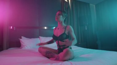 Siyah iç çamaşırı birçok dövmeler ile genç çekici kadın nilüfer oturarak yatakta poz ve bekliyor