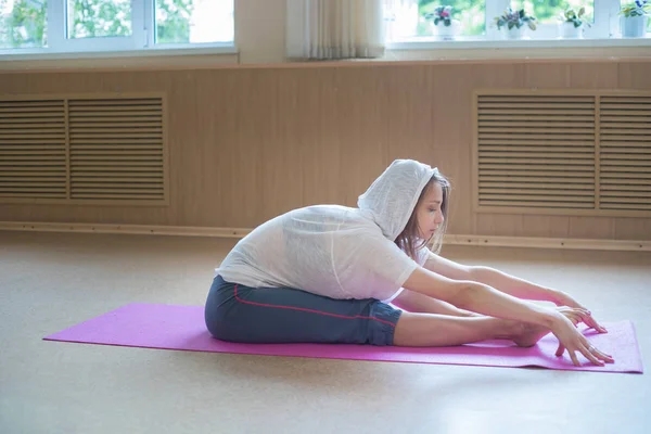 Junge schlanke Frau mit blonden Haaren sitzt auf der Yogamatte und beugt sich nach vorne — Stockfoto