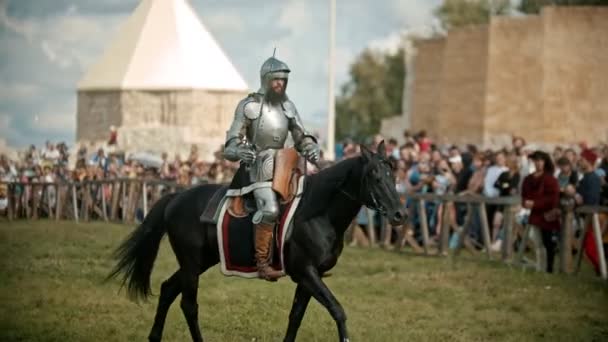 Bulgar, russland 11-08-2019: ein männlicher Ritter mit geöffnetem Helm reitet auf einem Pferd über das Schlachtfeld - Menschen beobachten hinter dem Zaun — Stockvideo