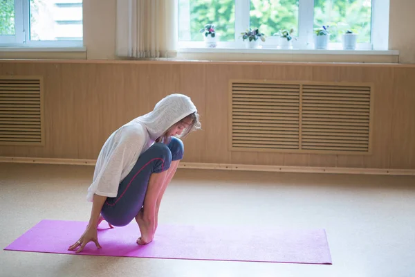 Junge Ballerina mit weißer Kapuze steht auf ihren Zehenspitzen auf der Yogamatte - Tanzstudio. — Stockfoto