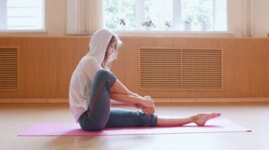 Genç ince kadın yoga mat üzerinde oturan ve lotus pozisyonda bacaklarını koyar