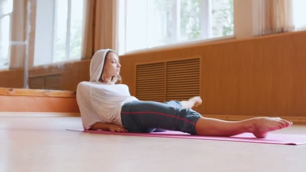 Mujer joven gimnasta acostada en el suelo y haciendo ejercicios en sus piernas estiramiento — Vídeos de Stock