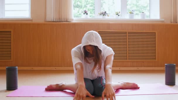 Mujer joven gimnasta calentándose en el suelo y haciendo ejercicios en sus piernas — Vídeo de stock