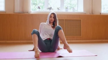 Genç kadın jimnastikçi yerde oturan ısınma ve stüdyoda germe egzersizleri yapıyor