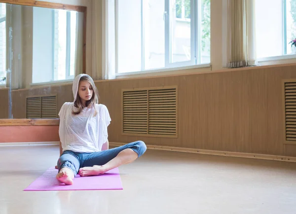 Junge hübsche Frau mit blonden Haaren sitzt auf der Yogamatte und schaut zur Seite — Stockfoto