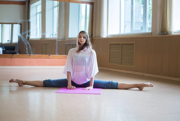 Giovane bella donna con i capelli biondi seduta nella spaccatura sul tappetino yoga — Foto Stock